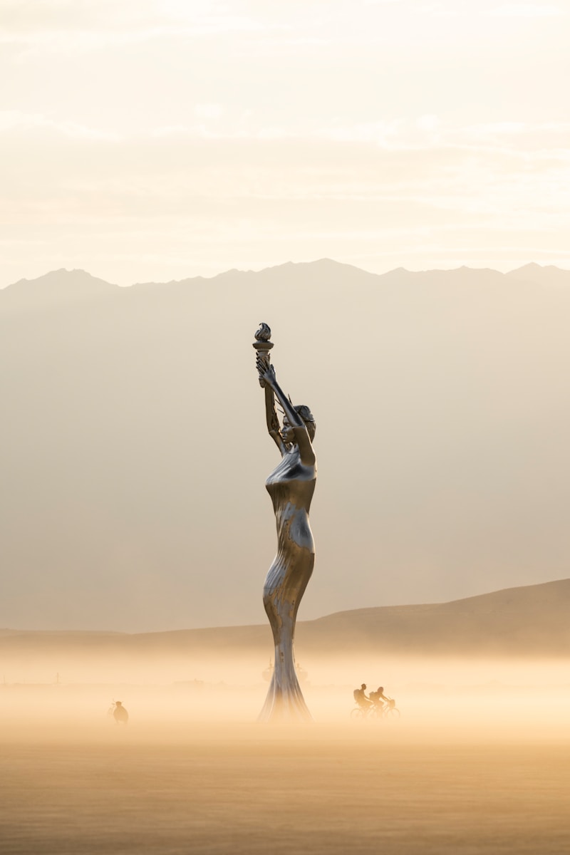 A statue in the middle of a desert with mountains in the background